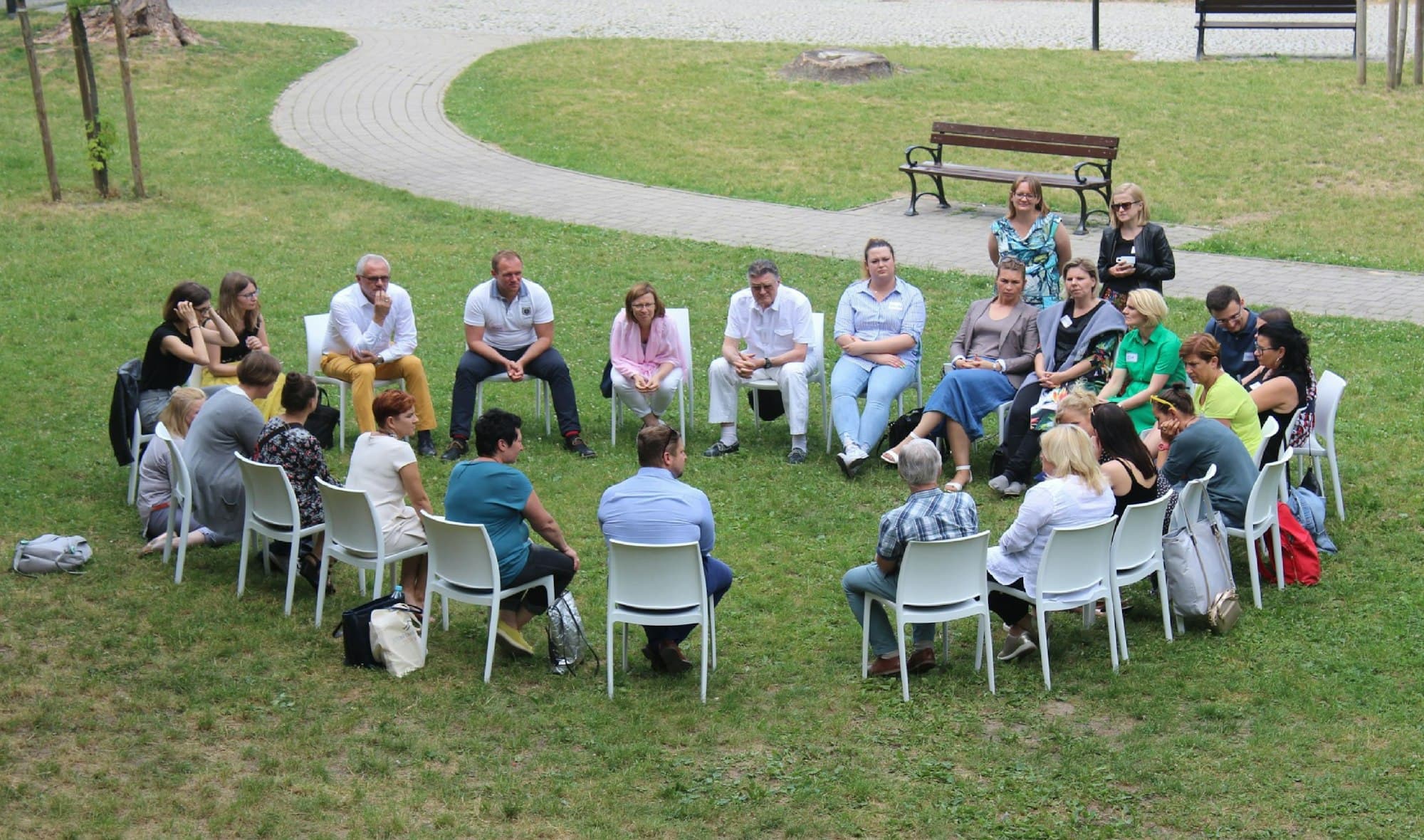 People sitting in a wide circle of chairs on a lawn, talking together